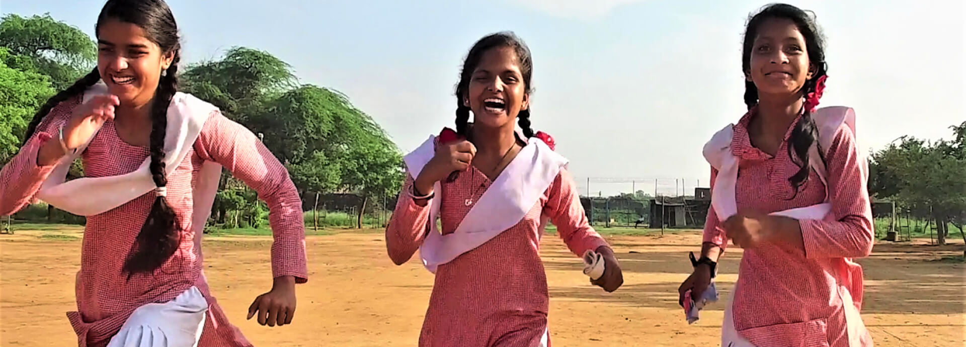 Three girls wearing pink dresses running while laughing