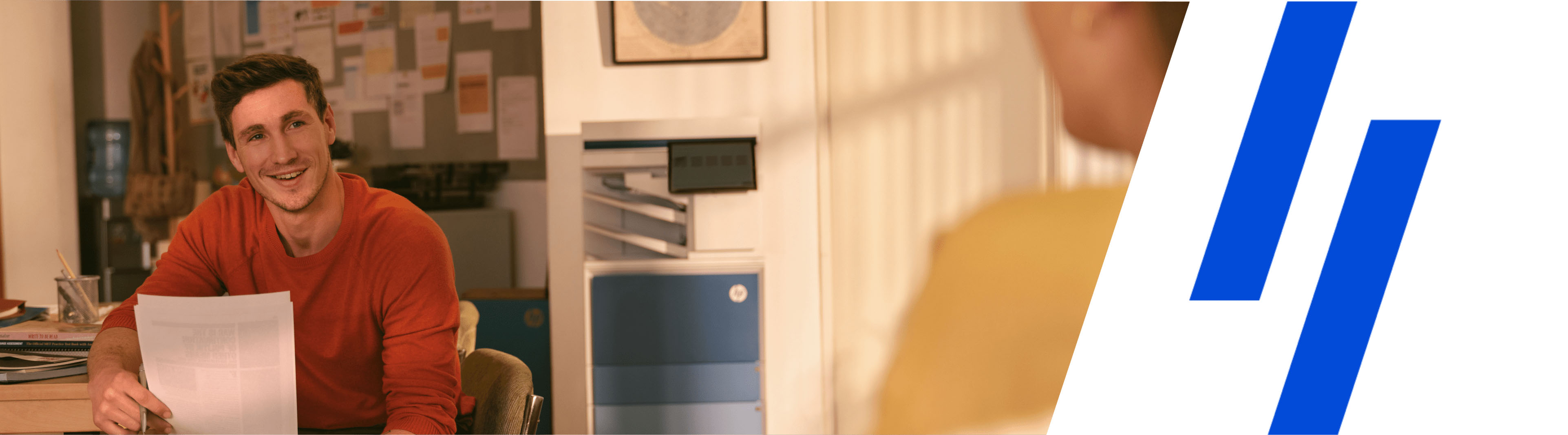 Image alt: Smiling man in creative office space holding printed documents with HP LaserJet Enterprise MFP to the right