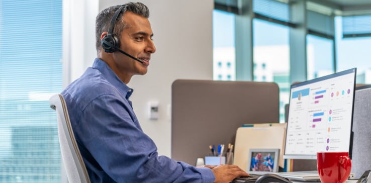 Man seated at office desk wearing Poly Savi 8210 headset while typing on keyboard and looking at Poly services screen on monitor Man seated at office desk wearing Poly Savi 8210 headset while typing on keyboard and looking at Poly services screen on monitor