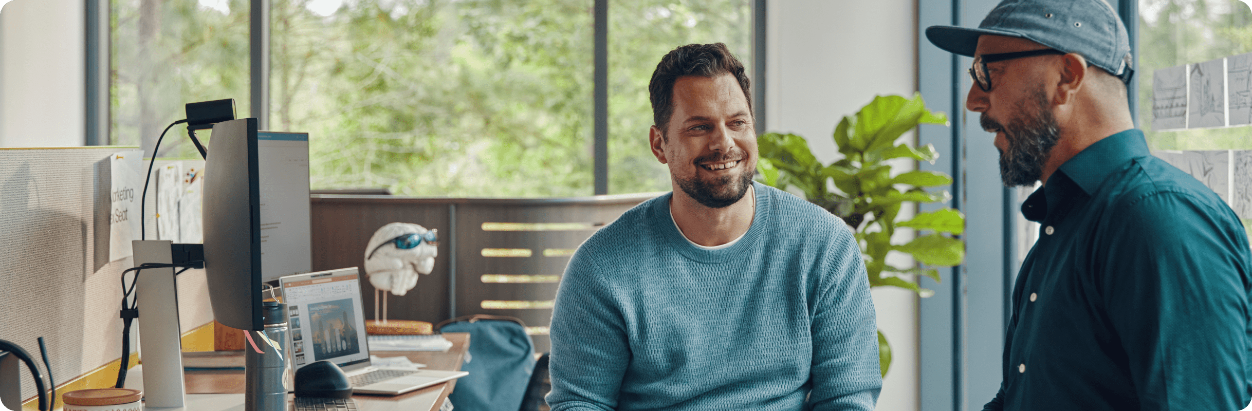 two men in light, bright office cubicle talking with HP curved dual monitors and HP laptop on desk